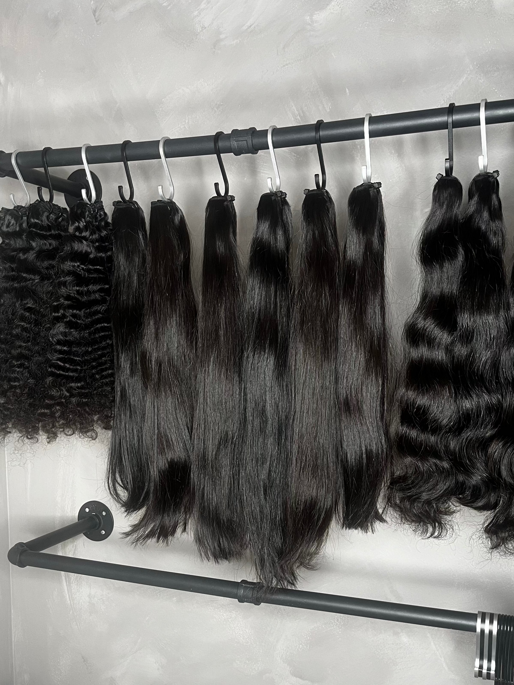 Collection of black hair extensions on a metal rack against a gray wall.